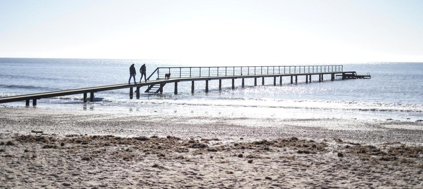 Par som går på stranden på vesterhavet ved en badebro