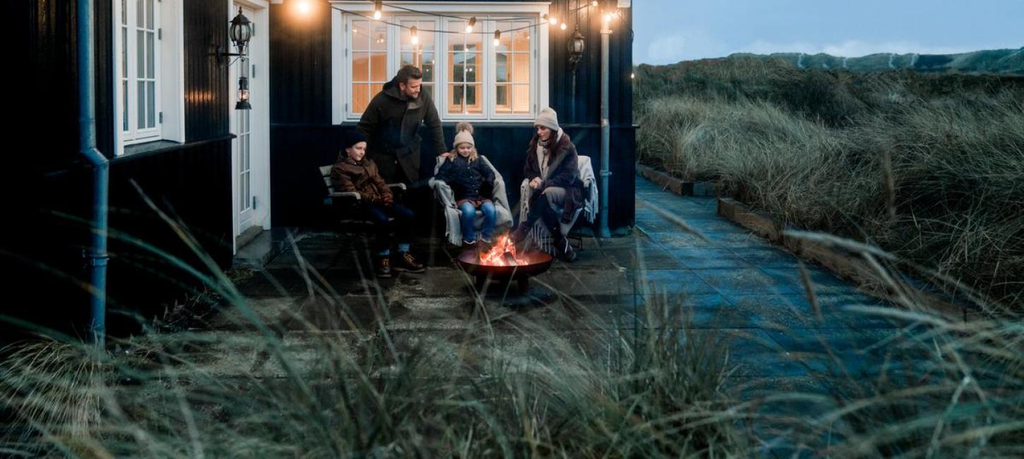 Familie sidder ved bål udenfor sommerhus