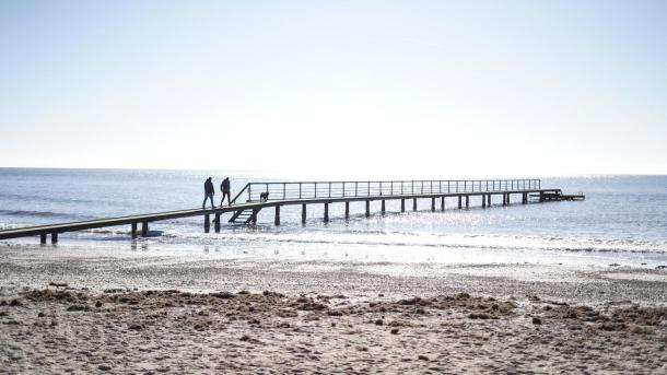 Par som går på stranden på vesterhavet ved en badebro