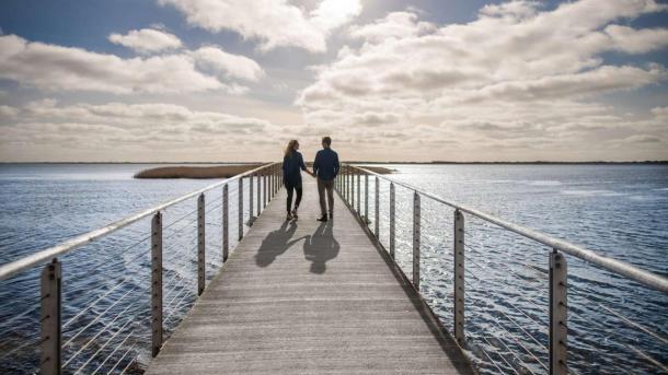 Et par som går ved vesterhavet på en bro på en smuttur