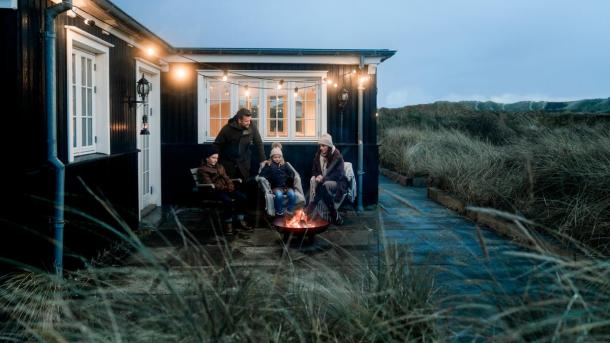 Familie sidder ved bål udenfor sommerhus