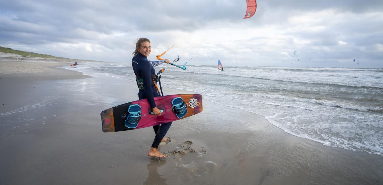 Pige står i strandkanten med kitesurf board