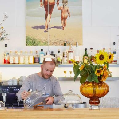 Mand i café med stort maleri af kvinde og barn på stranden