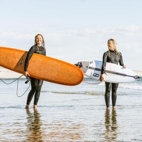 To damer som står i vandkanten med deres surfboards