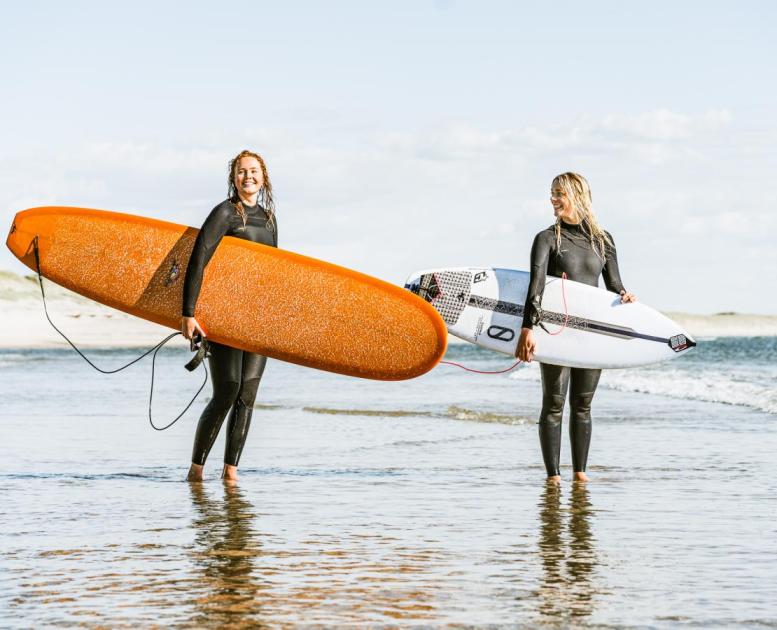 To damer som står i vandkanten med deres surfboards